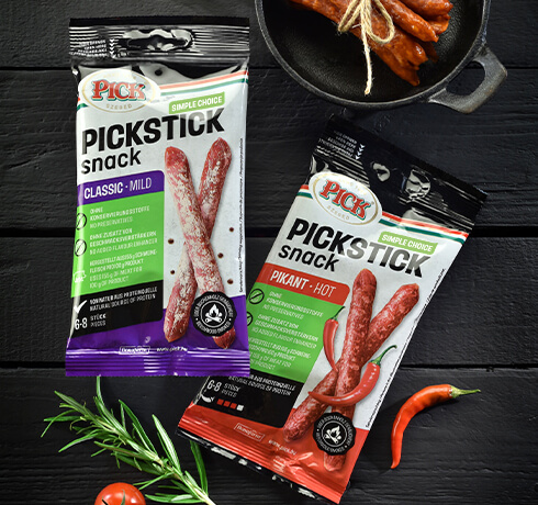 Verpackungen von PICKSTICK mild und pikant nebeneinander auf einem Holzuntergrund